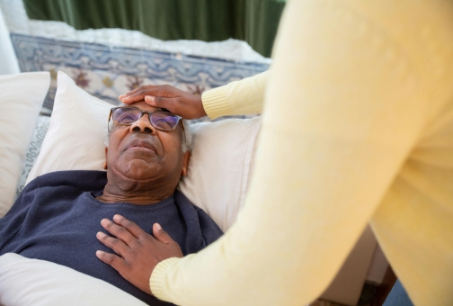 catholic care of the elderly man in bed while a visitor takes his temperature